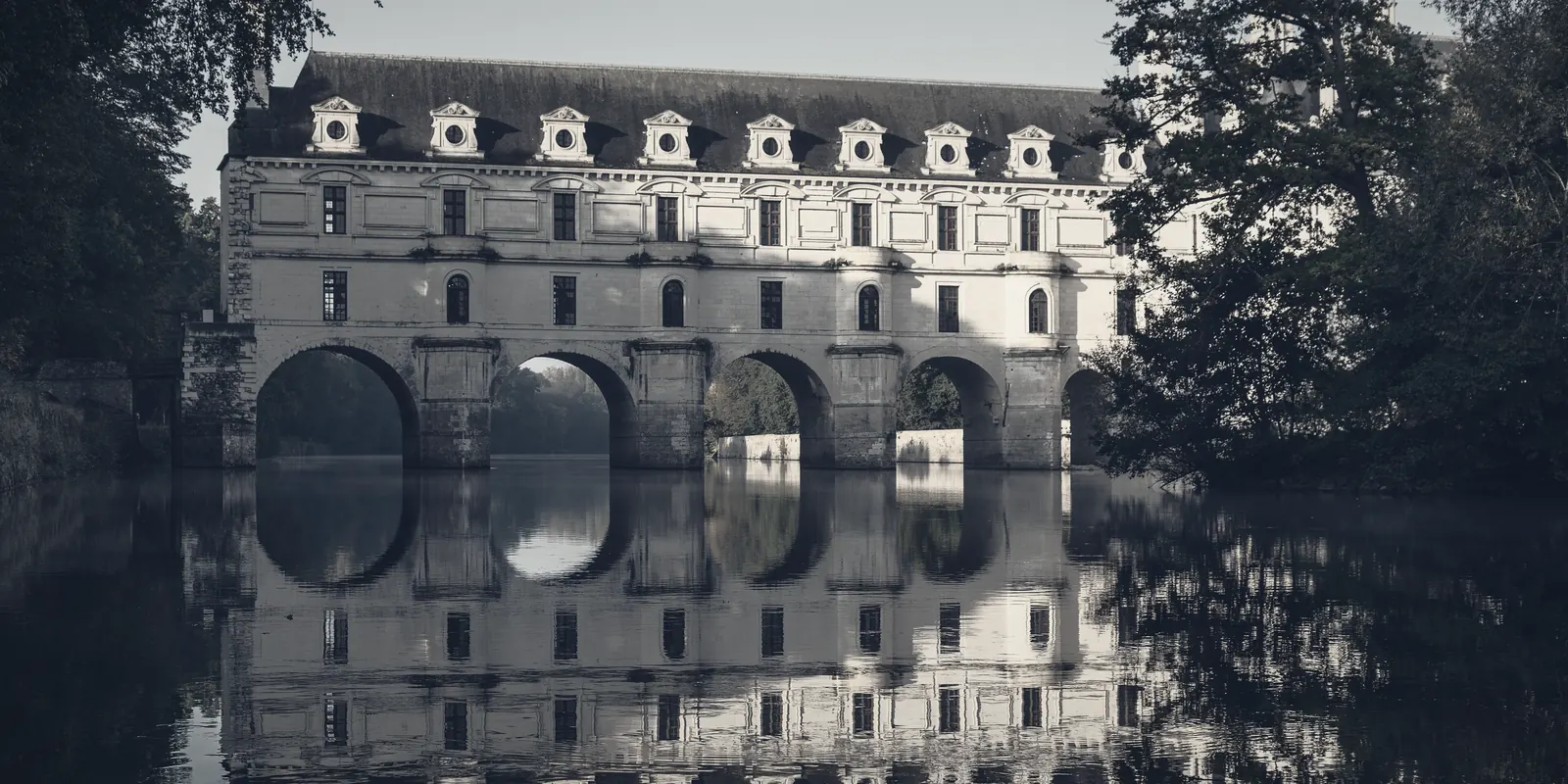 A renaissance chateau built out across the water, reflected beneath its arches