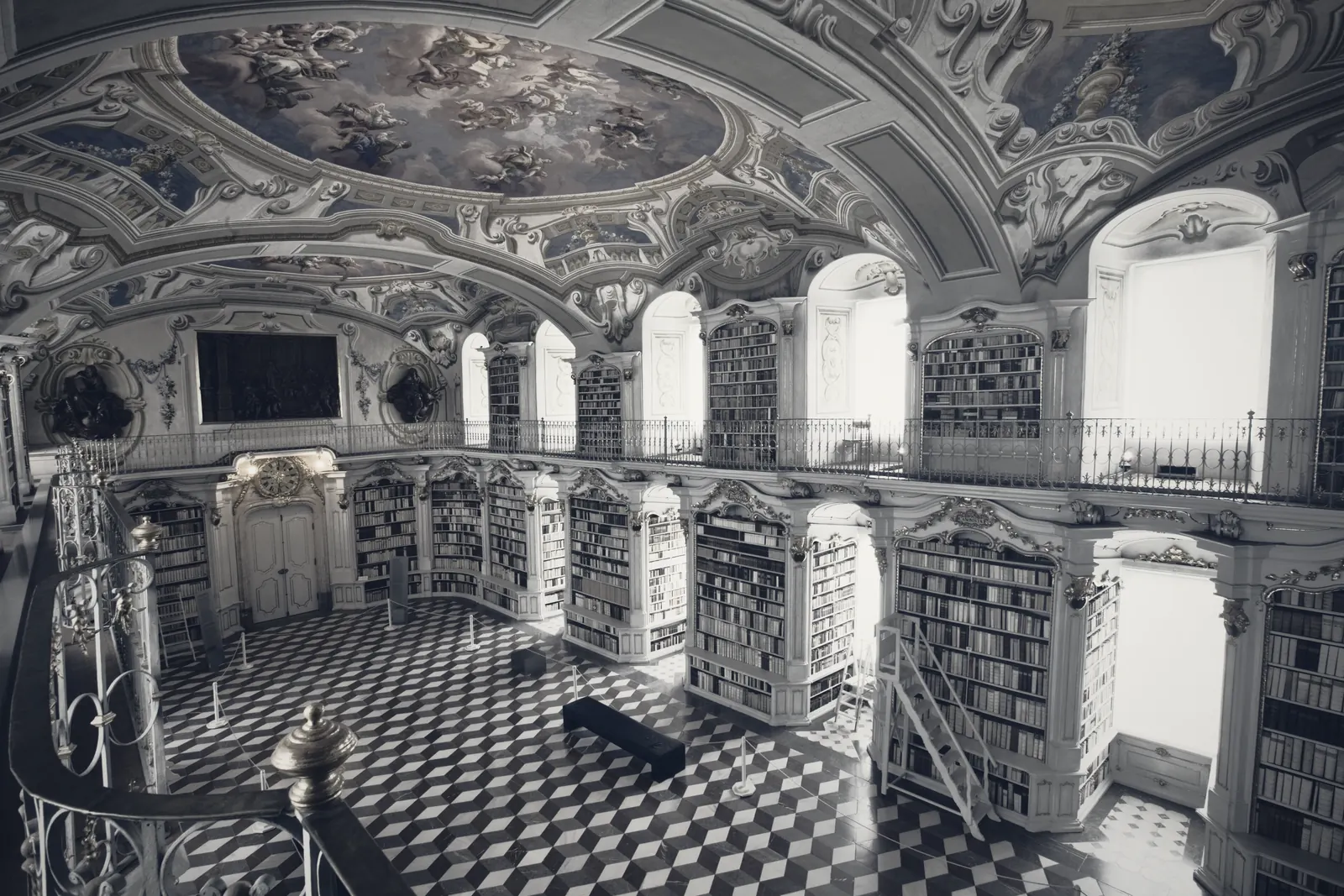 The nave of a baroque abbey library beneath a painted ceiling